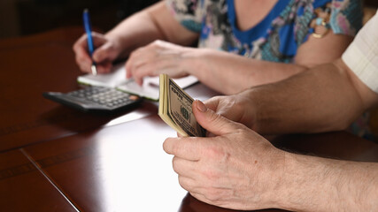 Man counting cash, woman writing down budget. Elderly spouses plan their expenses