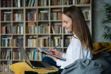 Woman with documents using a laptop at home against the background of a rack of books