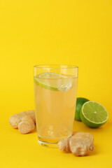 Glass of ginger beer and ingredients on yellow background