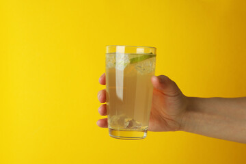 Female hand hold glass of ginger beer on yellow background