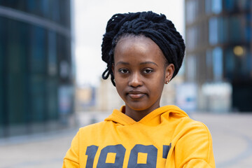 portrait of calm confident fashionable young black lady, beautiful trendy african american woman with dreadlocks in yellow clothes, serious afro student girl smiling at college, university outdoors.