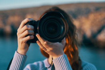 woman holding a camera with a lens in nature in the mountains and the sea in the background