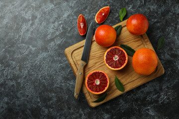 Board with red oranges, leaves and knife on black smoky table