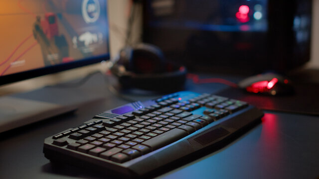 Close up of professional RGB keypad in empty gaming room prepared for streaming online tournament, display with first person shooter playing on it. Game studio with powerful computer