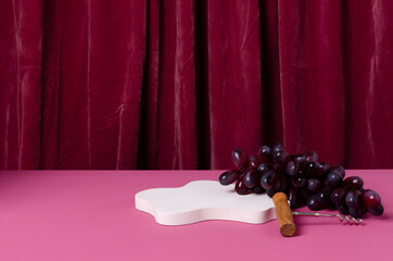 White stand for product show, corckscrew and grape on the pink table against dark red...