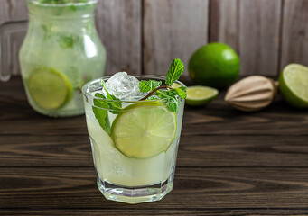 Homemade lemonade with lime, mint in a glass with a jug on a wooden rustic table.