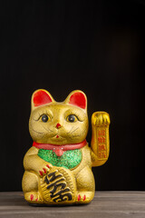 Close-up of golden maneki neko on wooden table and black background, vertical, with copy space