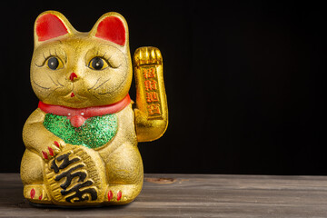 Close-up of golden lucky cat with green and red tones, on dark wooden table, black background, horizontal, with copy space