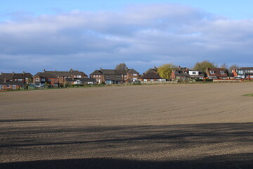 Obraz premium Farmers ploughed field on the edge of a housing estate with blue sky