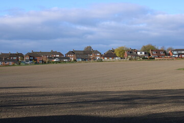 Farmers ploughed field on the edge of a housing estate with blue sky