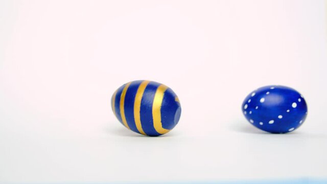 Easter eggs are rolling, knocking each other on white table. Eggs trendy colored classic blue, white and golden . Happy Easter. Minimal style
