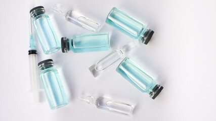 Vial vaccine, top view of glass ampoules with transparent and blue liquid lying on white background, global vaccination concept