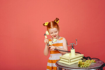 Little girl with red hair talking on the phone on a pink background.