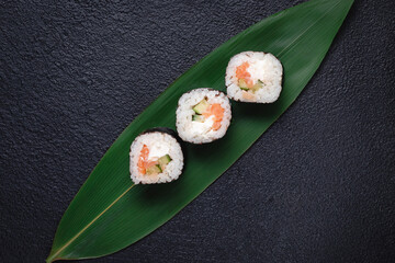 Classic sushi rolls on a bamboo green leaf on a dark background