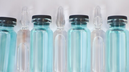 Vial vaccine, top view of glass ampoules with transparent and blue liquid lying on white background, global vaccination concept
