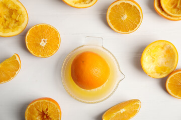 Fototapeta na wymiar Squeezer and cut fresh oranges on white wooden table, flat lay