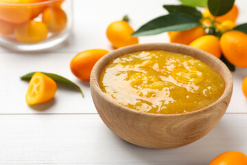 Delicious kumquat jam in bowl and fresh fruits on white wooden table, space for text