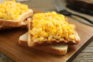 Delicious breakfast with scrambled eggs and toasted bread served on wooden board, closeup