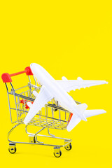 Flight sale concept. Vacation travel tour. Tourism opening. Plane in a shopping cart on trendy yellow background. Cheap flights.