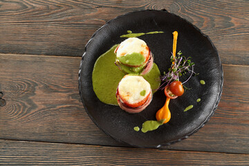 From above view of healthy baked vegetables and ham sandwiches with cheese on top served with pesto sauce, egg yolk, fresh sprouts and cherry tomatoes. Black plate on wooden table.