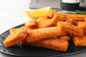 Tasty fresh fish fingers on black plate, closeup