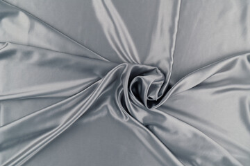 Gray silk or satin fabric is used as a 3D background. Abstract background in the form of a snail-twisted to the center and with shiny silvery folds diverging in different directions. Fabric sample.