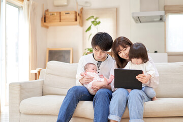 ソファに座ってのタブレットを見るアジア人ファミリー