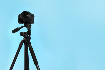 Modern tripod with professional camera on light blue background. Space for text