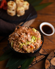 hot second courses of Japanese cuisine. Chahan rice with shrimp and vegetables in a black bowl on a table with bamboo leaves and soy sauce in a white porcelain saucer