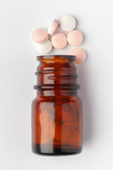 Macro Close up of medicinal or herbal pink white pill spilled and in an amber glass bottle. Top view, white background.