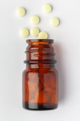Macro Close up of medicinal or herbal pale yellow pill in pill spilled and in an amber glass bottle. Top view, white background.