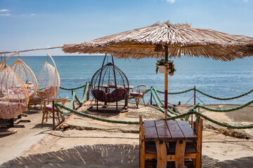cafe by the sea, restaurant on the beach, thatched beach umbrellas, table, wicker swing chair, rocking chair. Crimean pier,