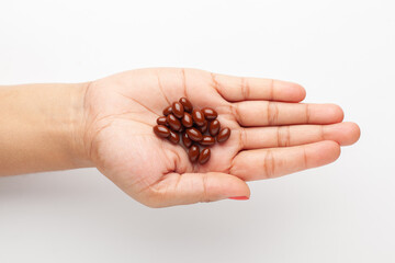 Macro Close up of medicinal or herbal dark red-brown pill on female hand palm. Top view, white background.