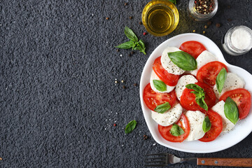 Caprese salad. Italian salad with fresh tomatoes, mozzarella cheese and basil on a dark background with copy space. Top view.