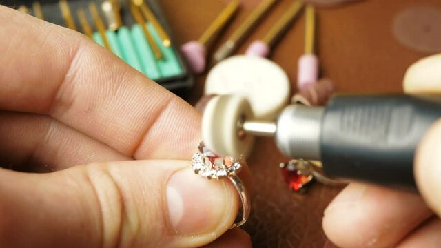 The jeweler is engaged in cutting a precious stone on a gold ring.A professional jeweler polishes a red gem on a gold ring using a special tool.