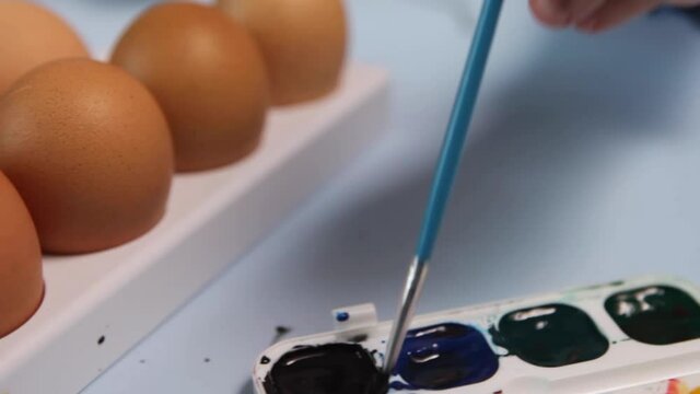 Child painting Closeup. The palette of colors is on the blue table. A child's hand holds a brush and mokes it in red High quality FullHD footage