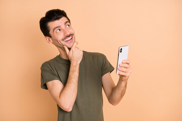 Photo portrait of man browsing internet with smartphone looking blank space dreaming thoughtful isolated on pastel beige color background