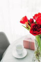 Bouquet of red tulips on table and white coffee cup. Concept for greeting card