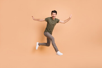 Fototapeta na wymiar Full length body size photo of jumping high guy smiling wearing checkered pants t-shirt isolated on pastel beige color background