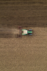Fototapeta na wymiar Aerial view of agricultural tractor tilling and harrowing ploughed field, directly above drone pov