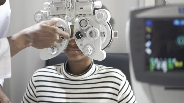 African teen girl doing eye test, Ophthalmologist examing eyesight measurement to young woman with phoropter at eyeglasses shop.
