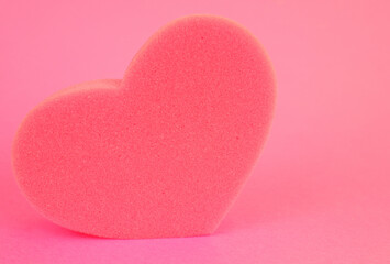 Fototapeta premium a washcloth, sponge in the shape of a pink heart on a pink background. Romantic background.