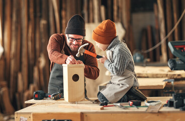 Kid with dad assembling wooden bird house in craft workshop - obrazy, fototapety, plakaty