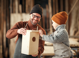 Kid with dad assembling wooden bird house in craft workshop