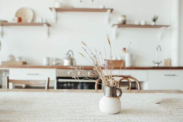 A vase with dry flowers on a table. Scandinavian classic kitchen with wooden and white details,...