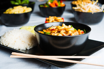 Thai food with chicken, cashew and vegetables in a dark bowl with other Thai dishes in the background