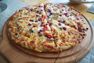 On a wooden dinner plate, delicious Russian pizza with blueberries, tomatoes, and ham.