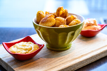 Baked fried potatoes in a nice bowl with sauce on the sides on a wooden board