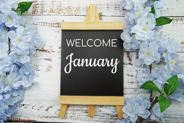 Welcome January text and blue flower decoration on wooden background