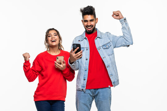 Portrait Of Indian Excited, Amazed Couple Looking On A Cell Phone Watching A Sports Game Match Or Reading An Sms, E-mail, Viewing Latest News, Isolated On A White Background.